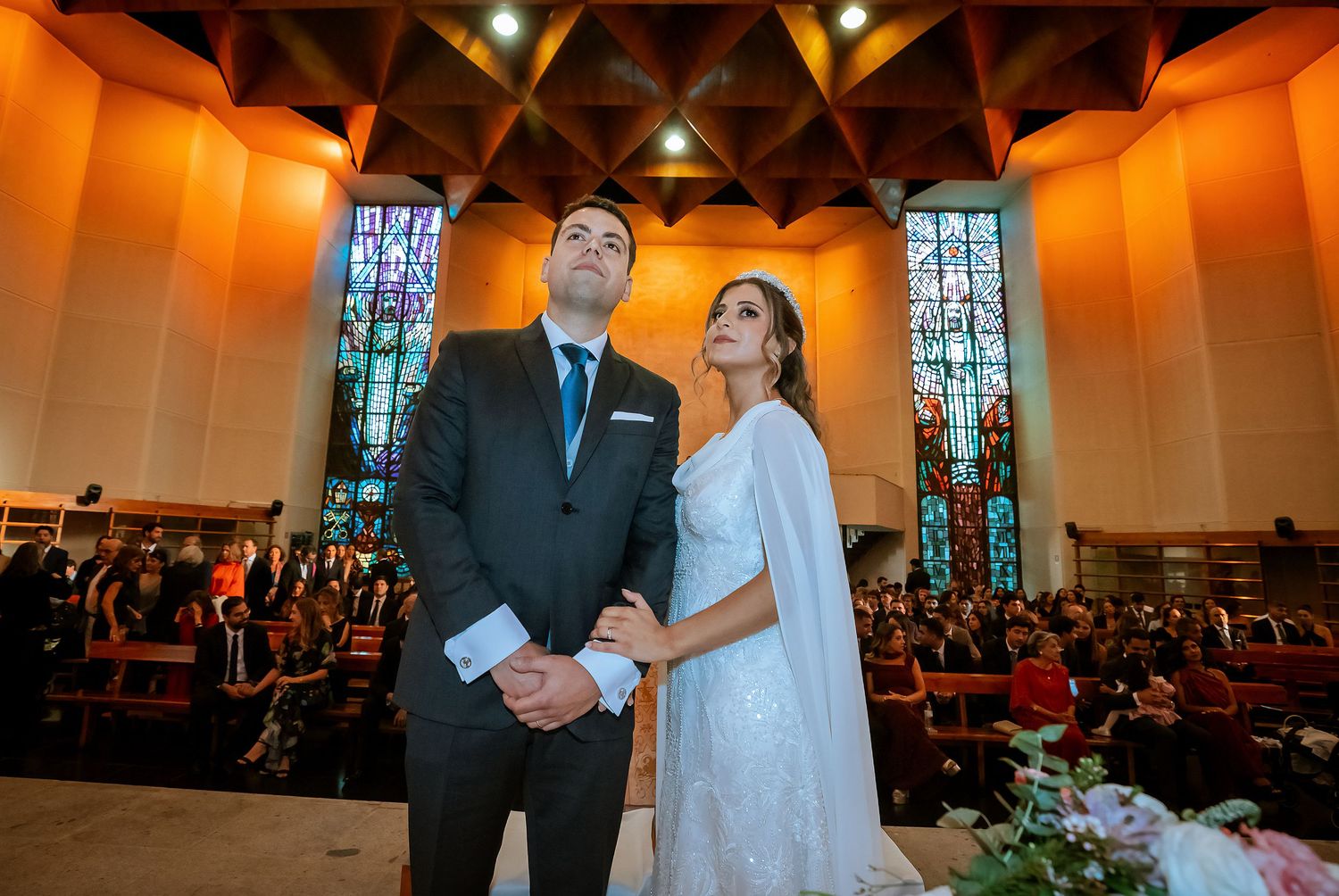 Bride and groom stand together at the altar, looking up during their Catholic wedding ceremony.