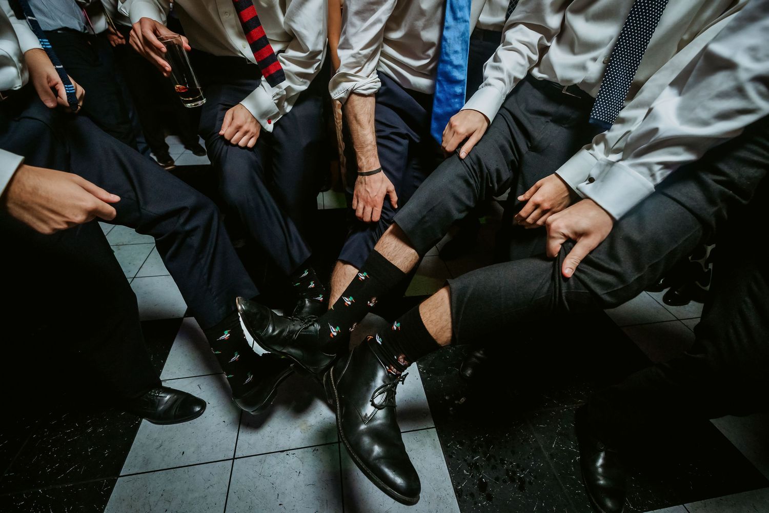 Groomsmen in formal suits showing off dress shoes and patterned socks at a wedding celebration.