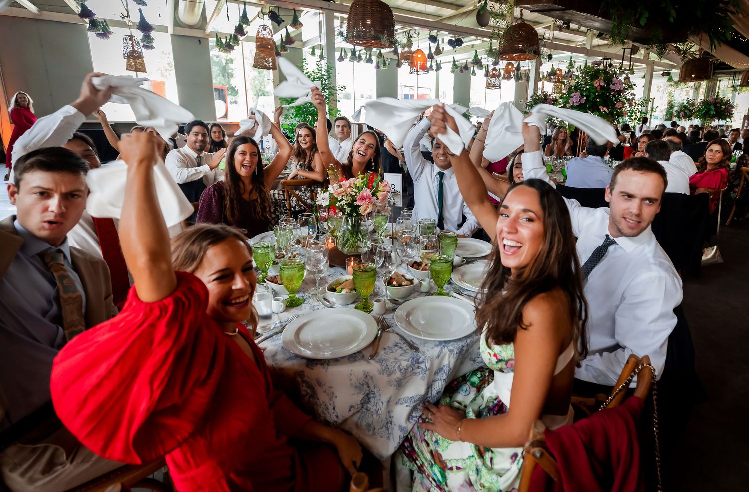 Joyful wedding guests waving white napkins at a festively decorated reception table.