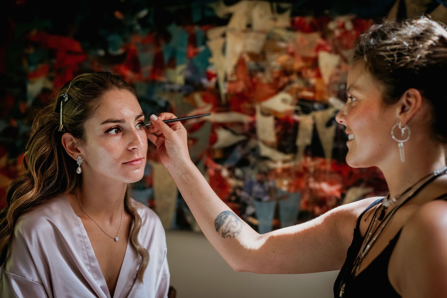 Professional makeup artist applying eyebrow makeup to bride wearing white robe before her wedding ceremony.