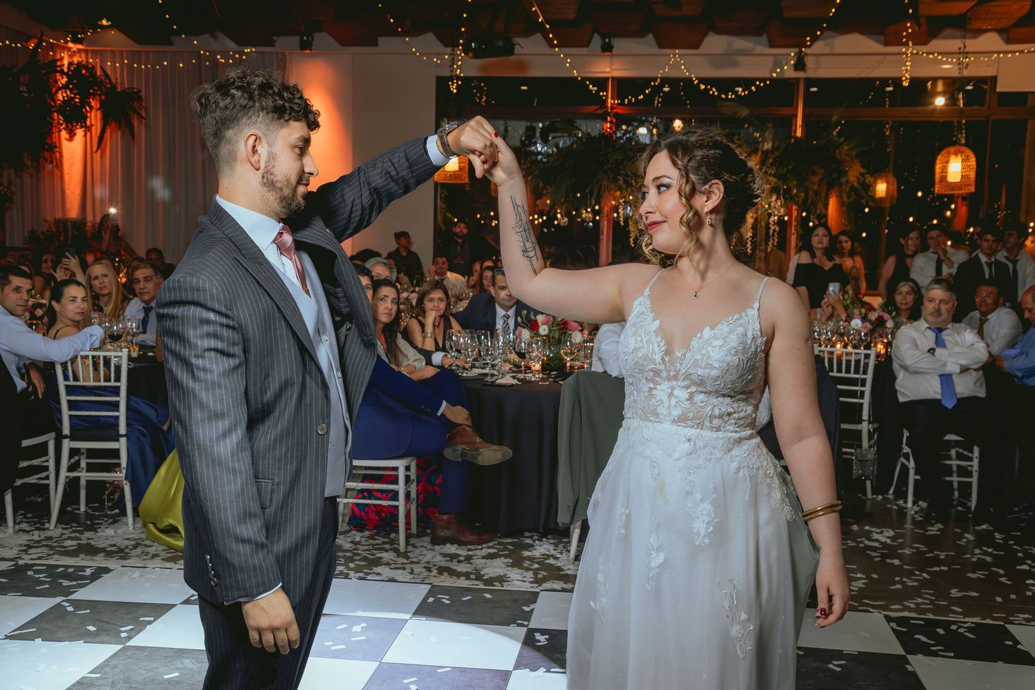 Groom spins bride in elegant wedding gown on checkered dance floor at romantic reception.
