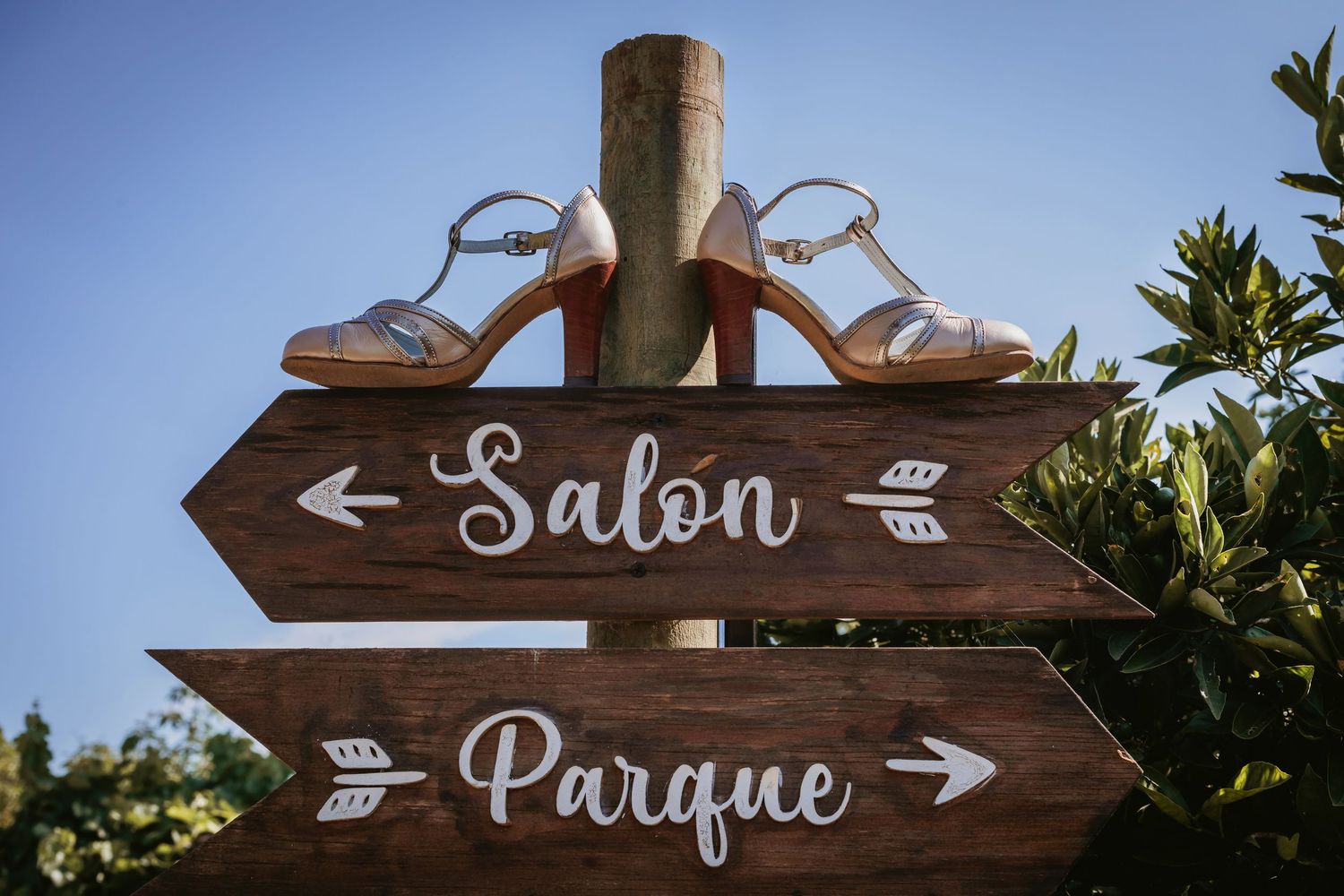 Bride's silver strappy heels displayed atop rustic wooden wedding directional signs for Salon and Parque.