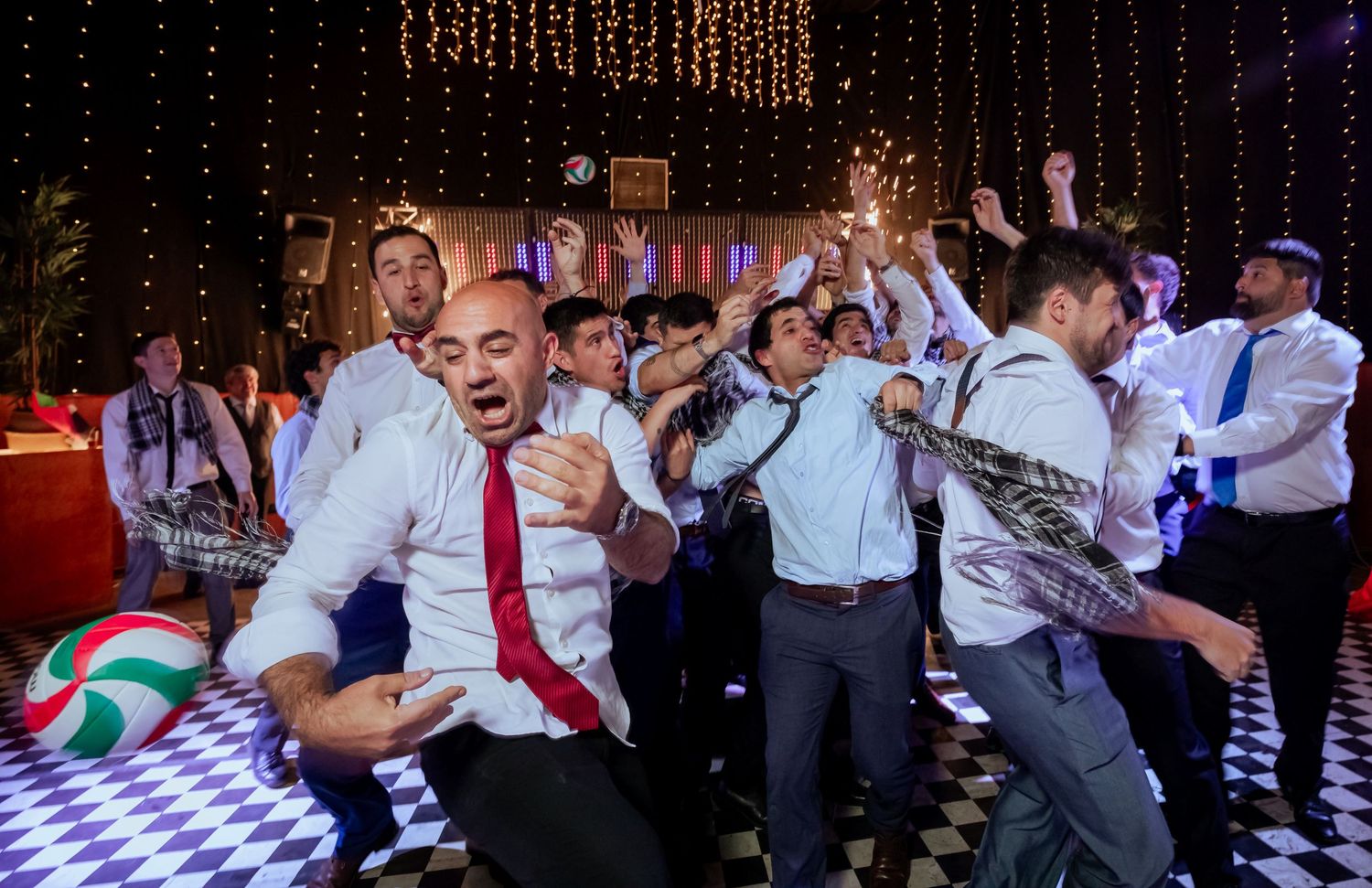 Groomsmen in white shirts dance energetically with sparklers on checkered floor at wedding reception.