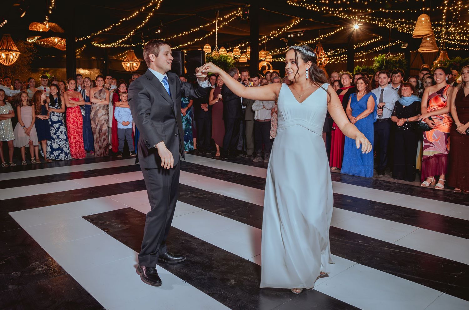 Bride and groom twirl together on checkered dance floor surrounded by cheering guests.