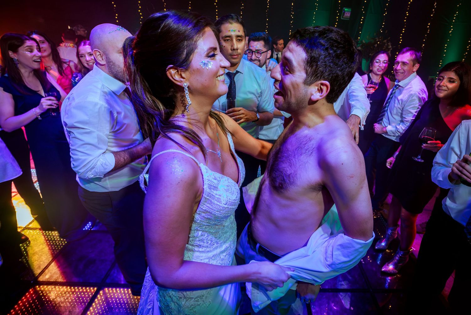 Couple dancing closely at a lively party, surrounded by guests on a colorful dance floor.