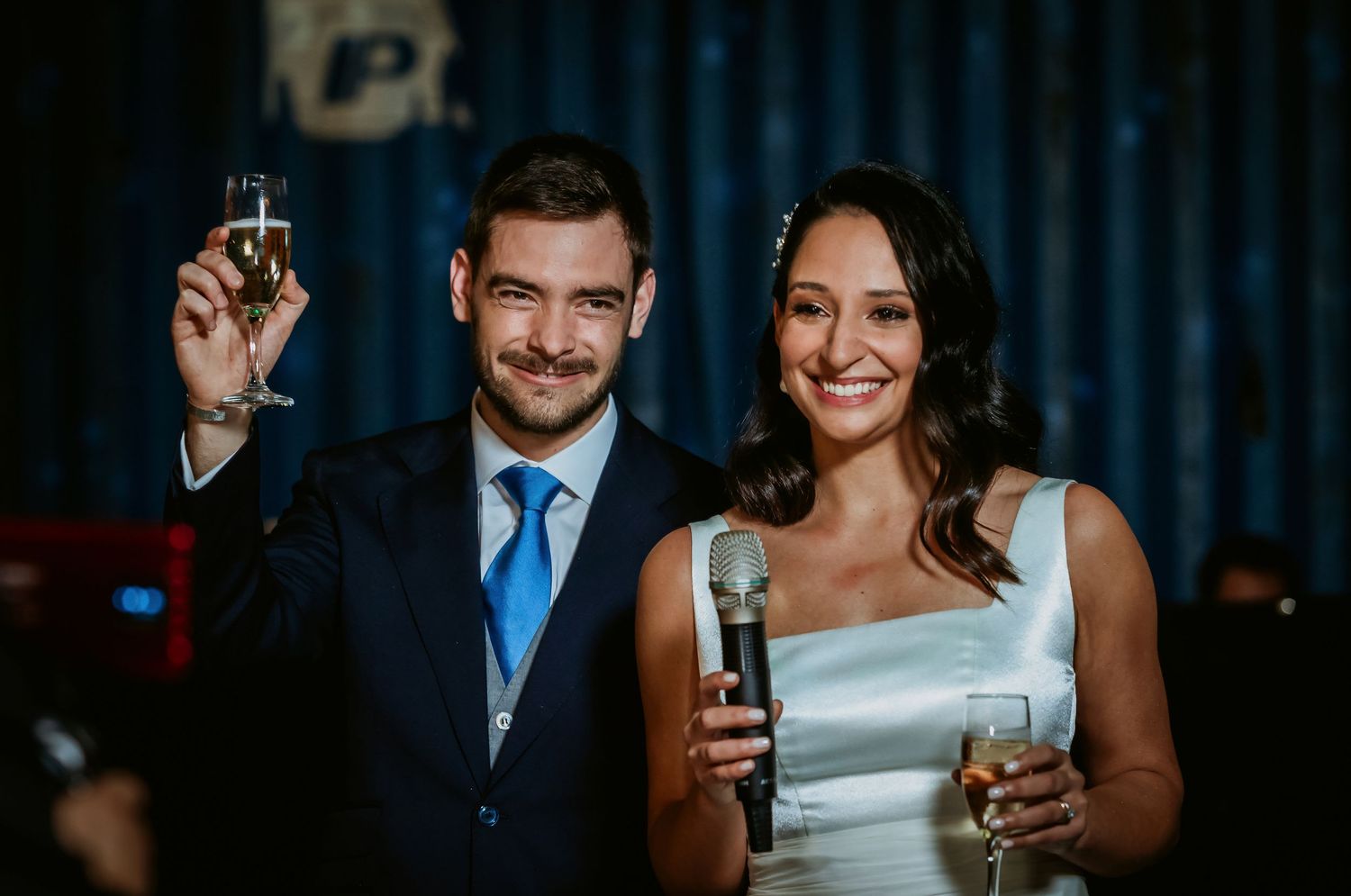 Bride and groom toasting with champagne glasses at their wedding reception, smiling joyfully.