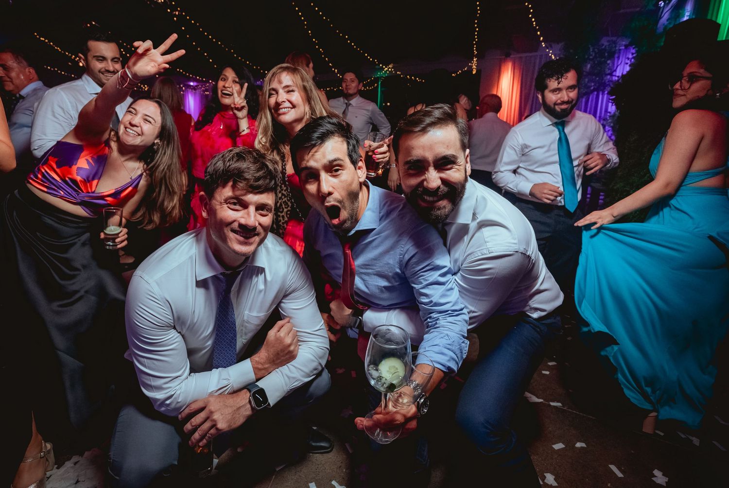 Three men pose playfully for a photo together at a festive wedding reception dance party.