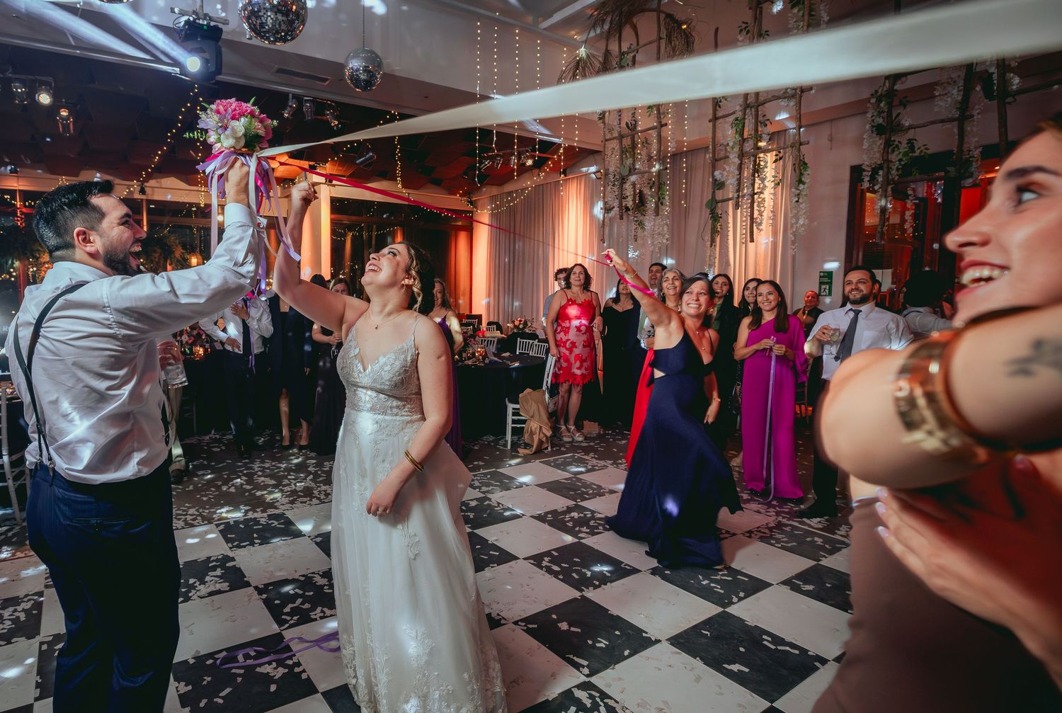 Bride tosses bouquet to eager guests on a festive wedding reception dance floor.