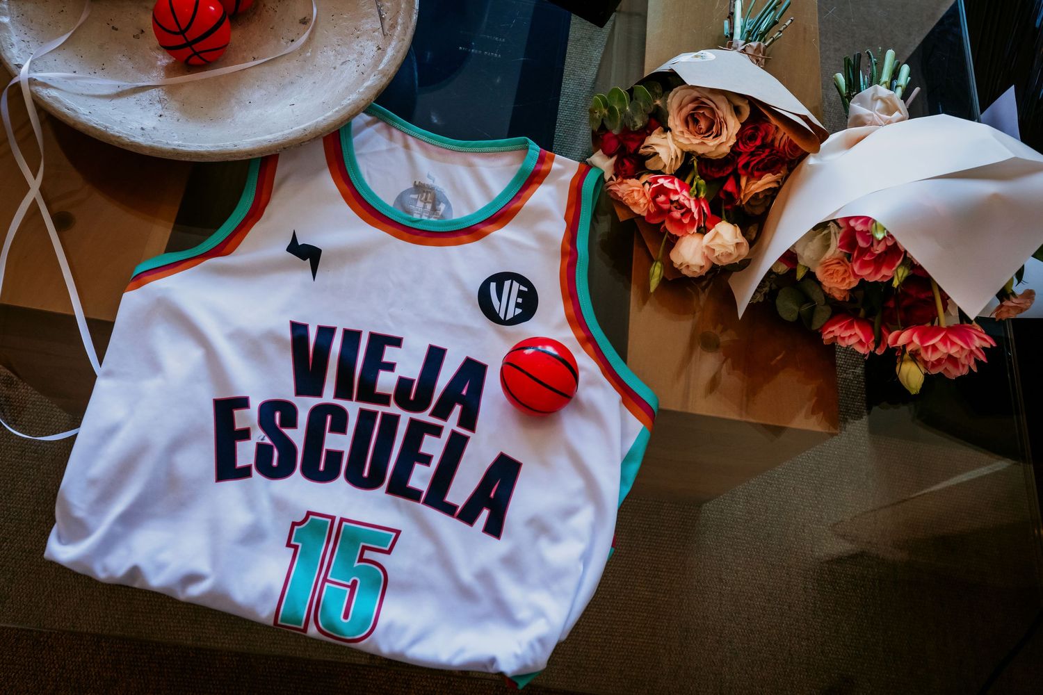 White basketball jersey reading Vieja Escuela number 15 displayed beside flowers.