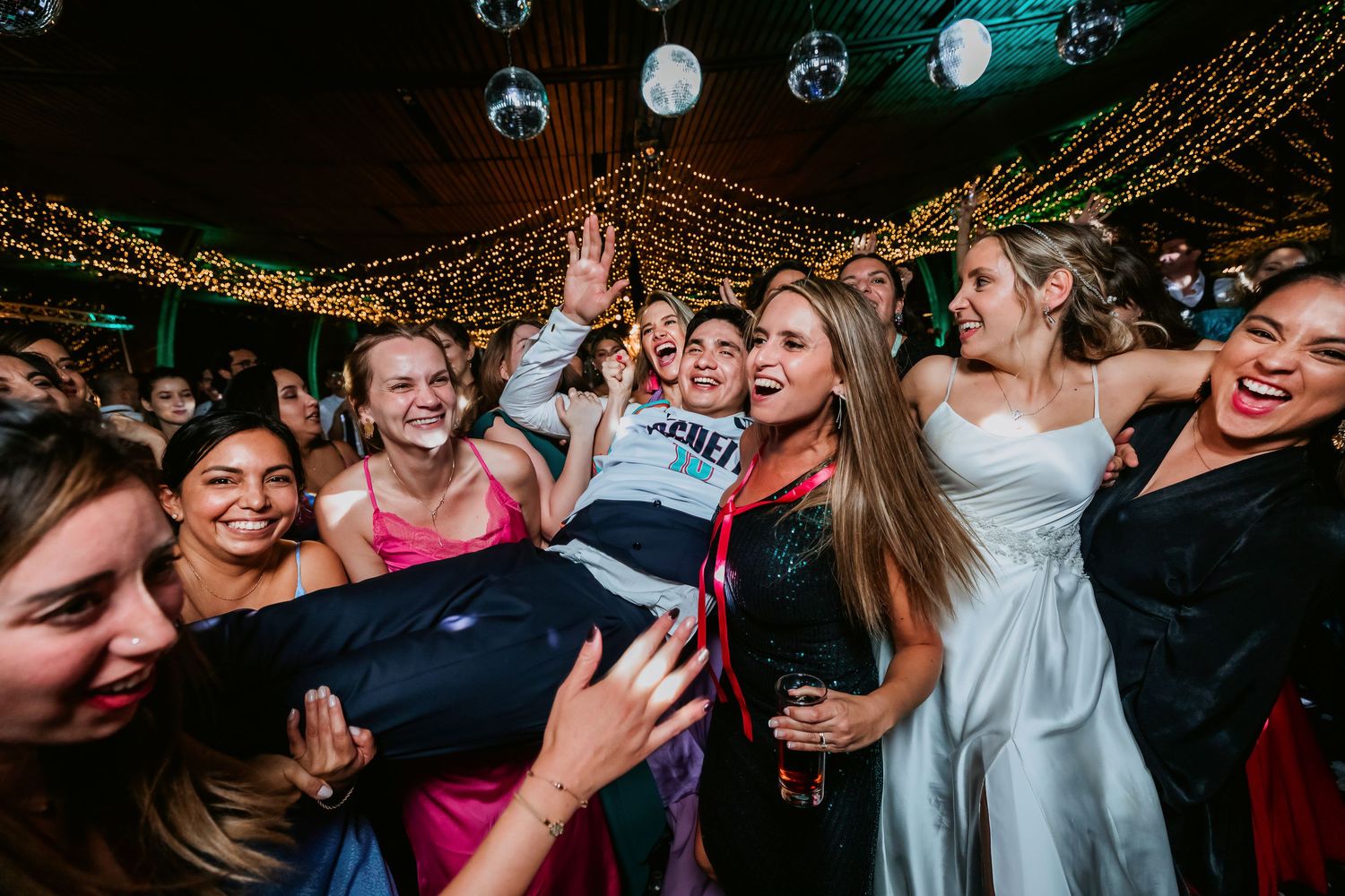Cheerful wedding guests surround the bride in a white dress on a festive dance floor.