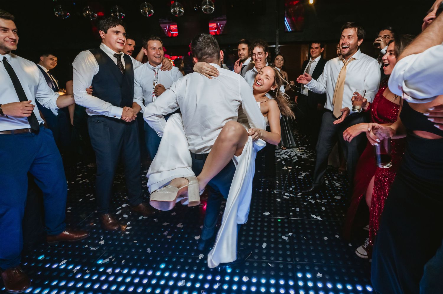 Bride and groom dancing energetically surrounded by cheering guests on a wedding dance floor.