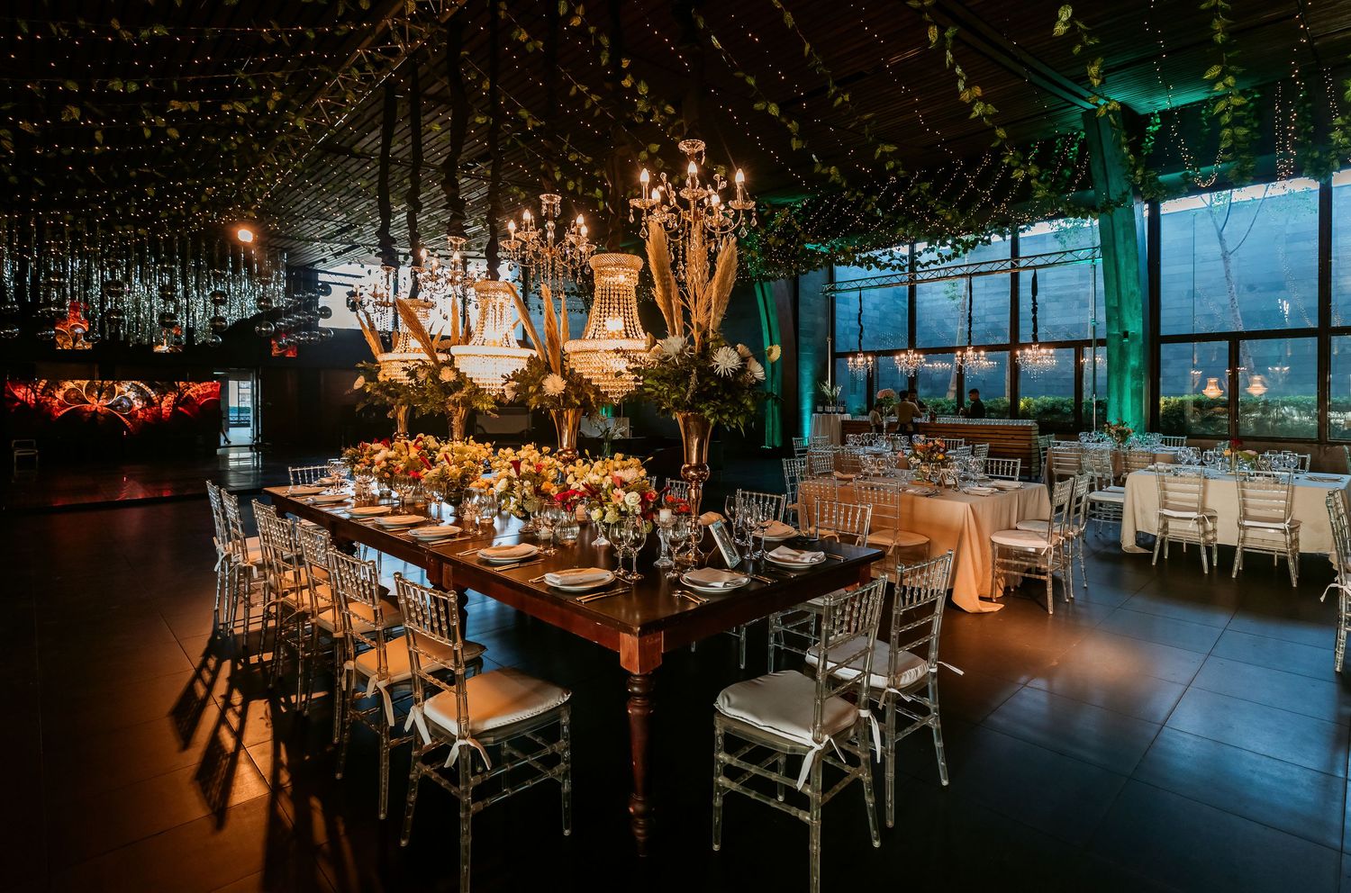 Romantic wedding venue with wooden tables, ornate chandeliers and lush floral arrangements.