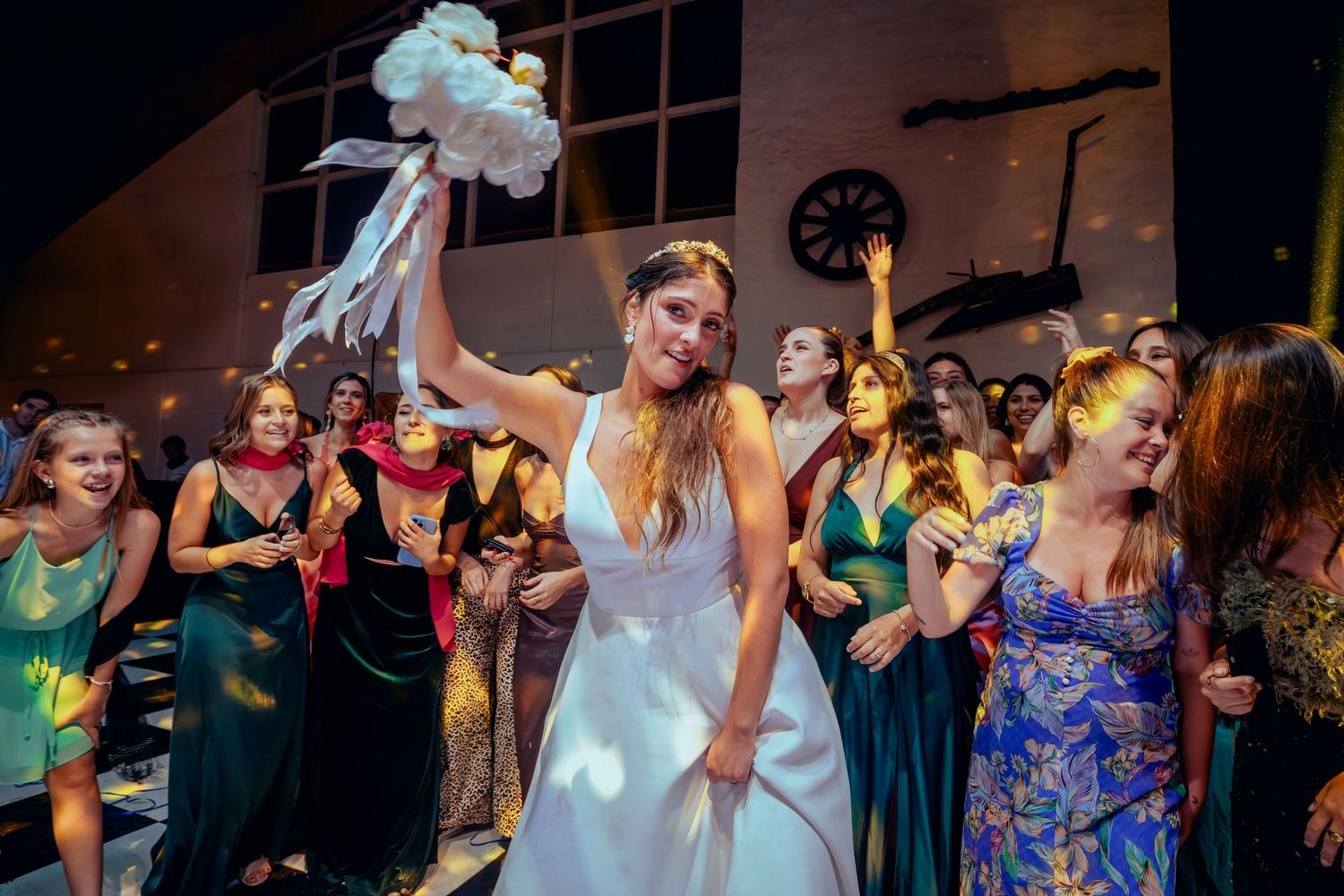 Bride tosses wedding bouquet to eager female guests at reception celebration.