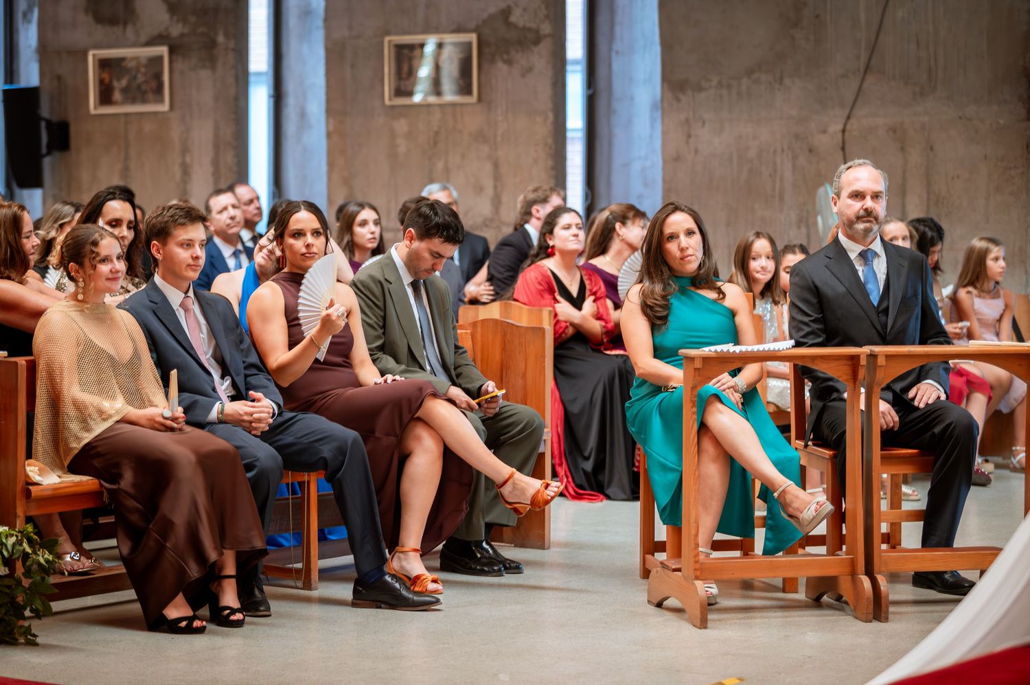 Elegantly dressed wedding guests seated in church pews during a Catholic wedding ceremony.