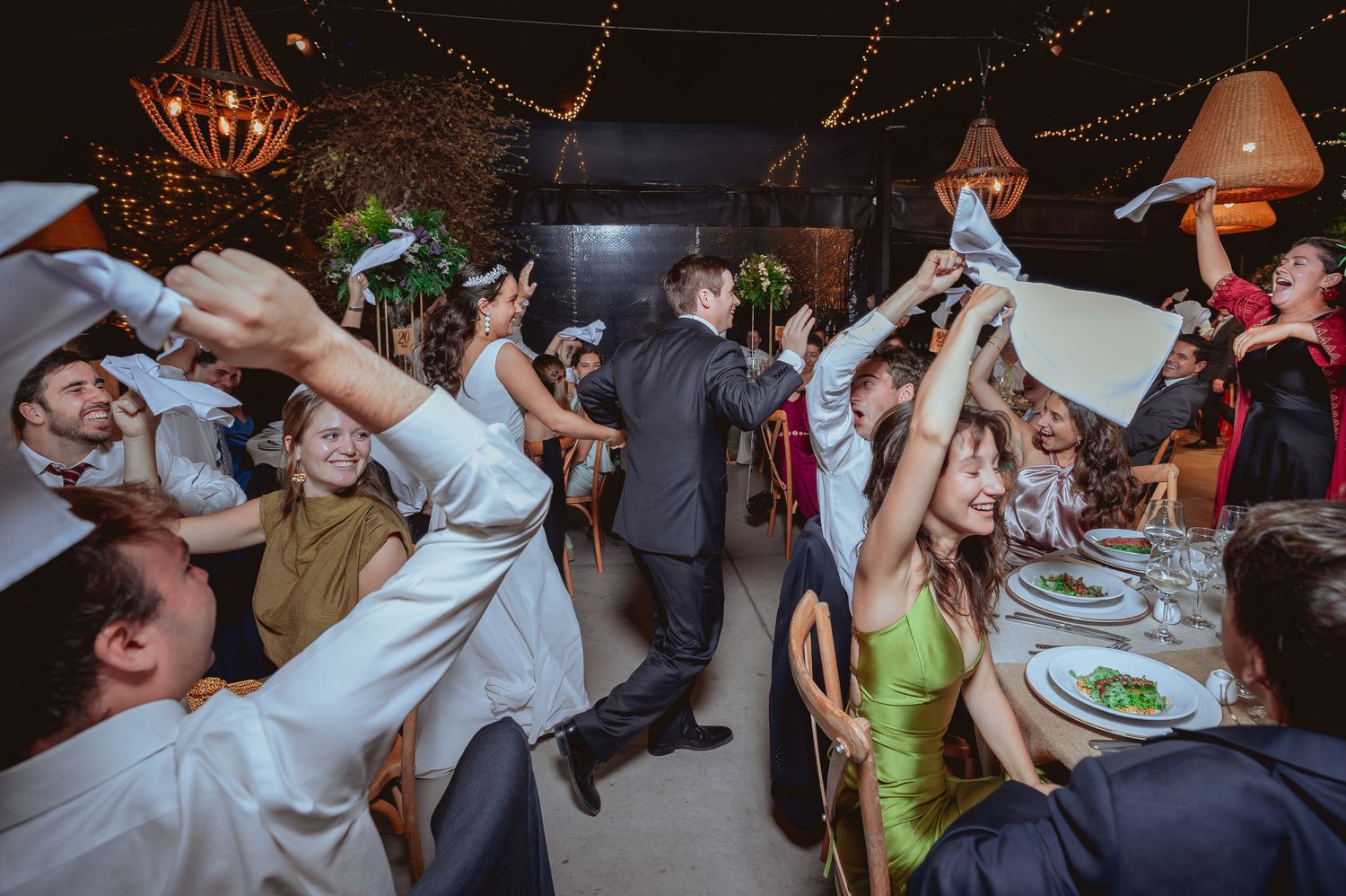 Joyful wedding guests wave napkins and dance around the couple during lively reception.