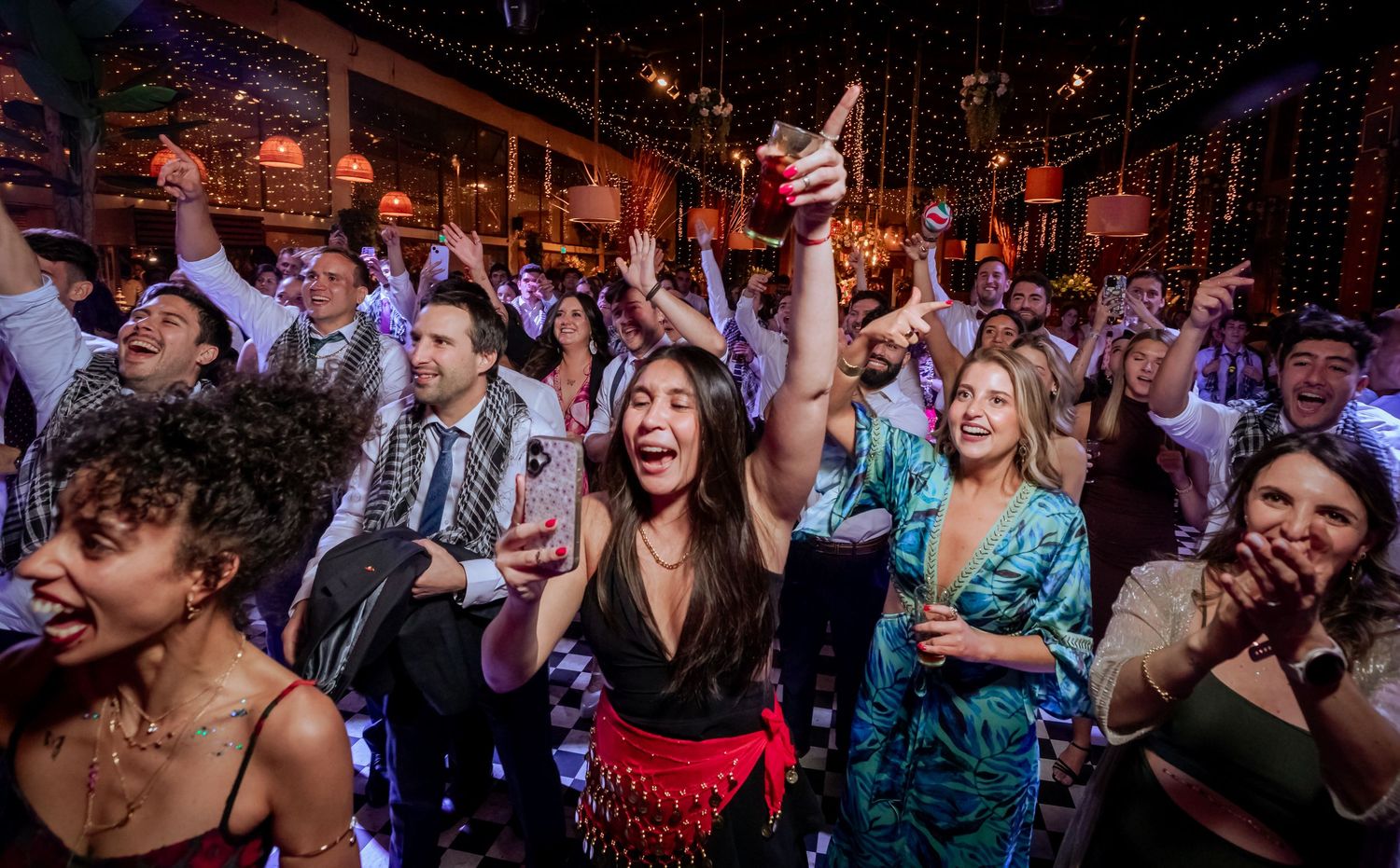 Joyful crowd of wedding guests cheering and dancing together at a lively wedding reception party.