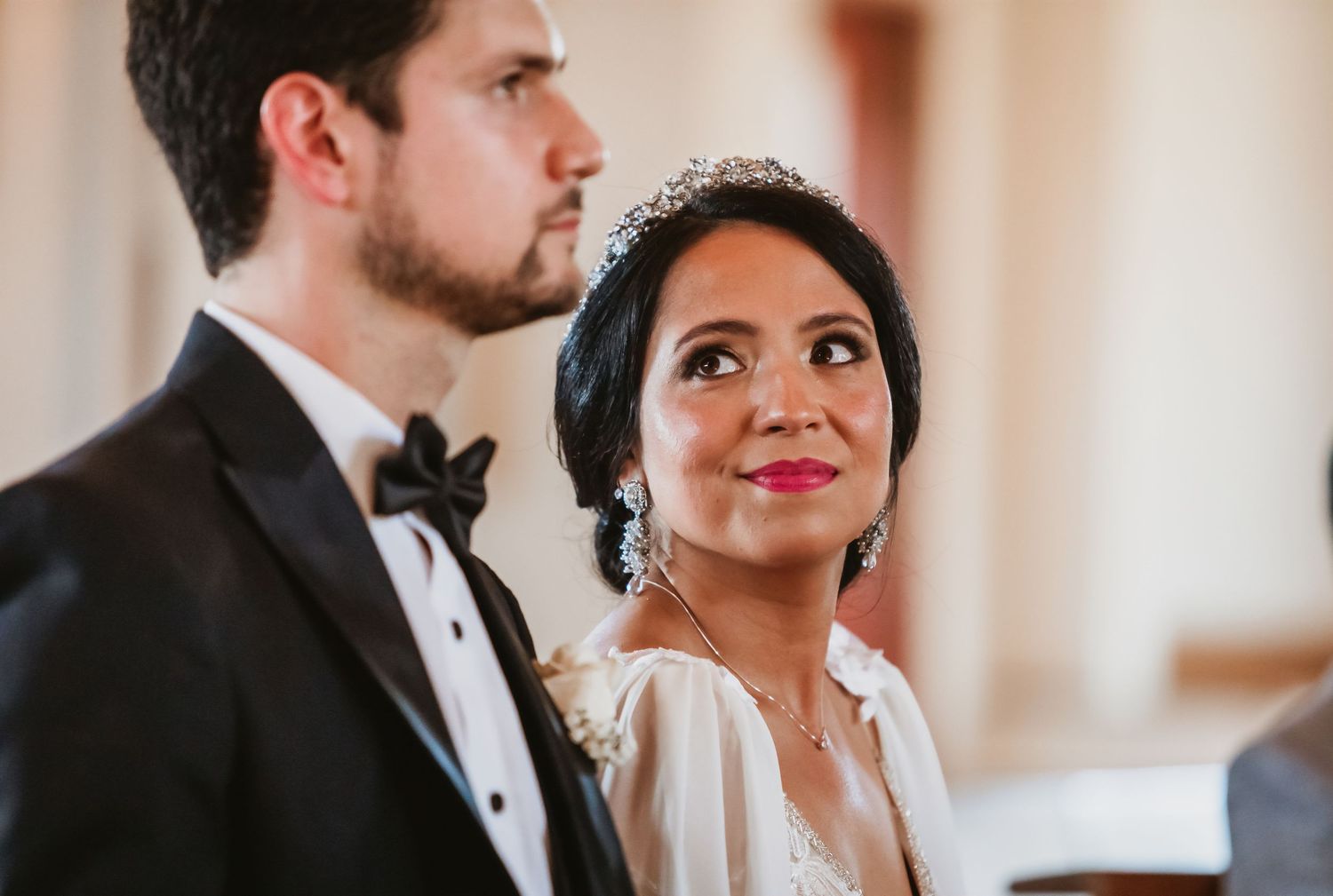 Bride wearing tiara and groom in tuxedo during wedding ceremony in church.