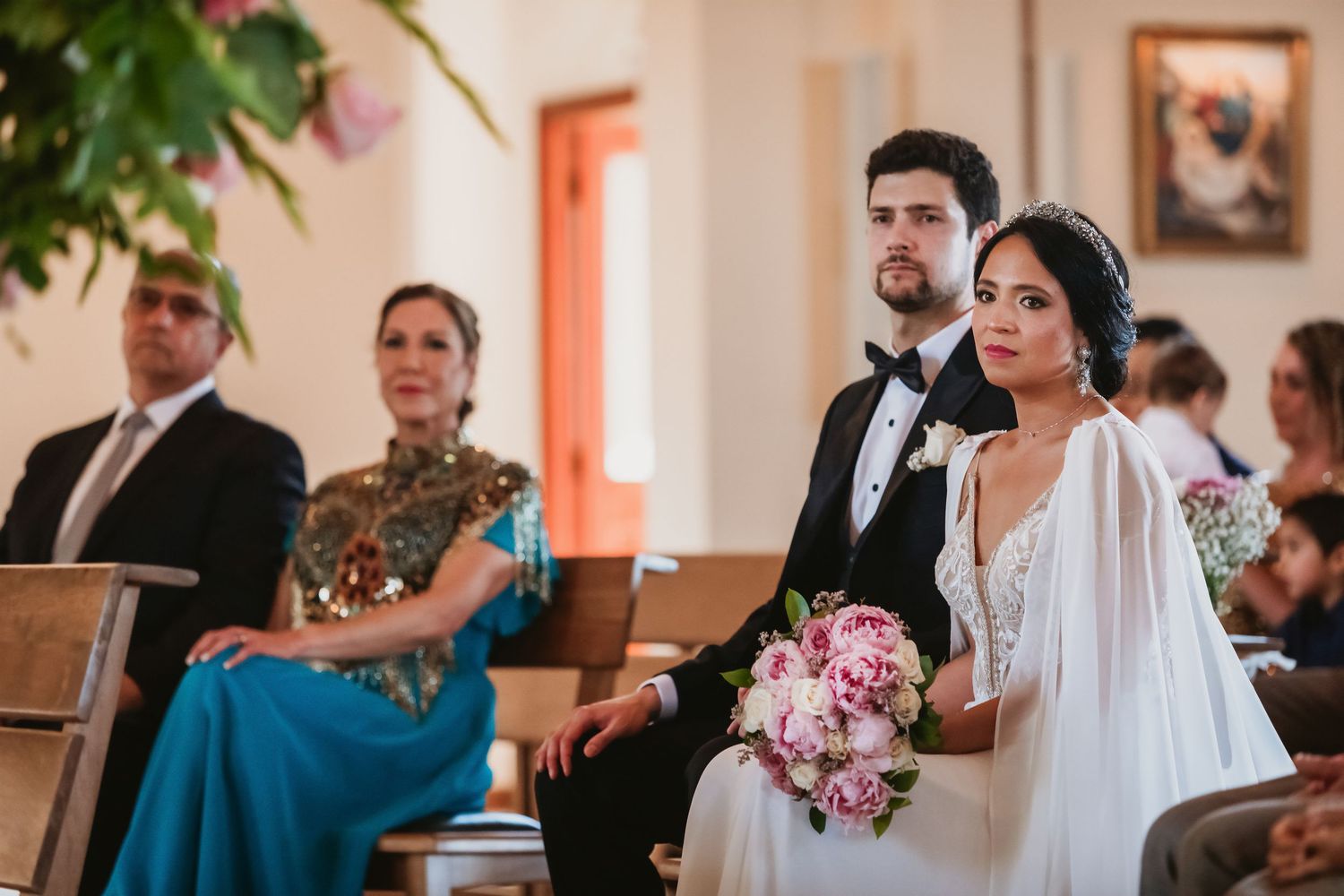 Bride and groom sitting together during wedding ceremony, bride holding beautiful pink peony bouquet.