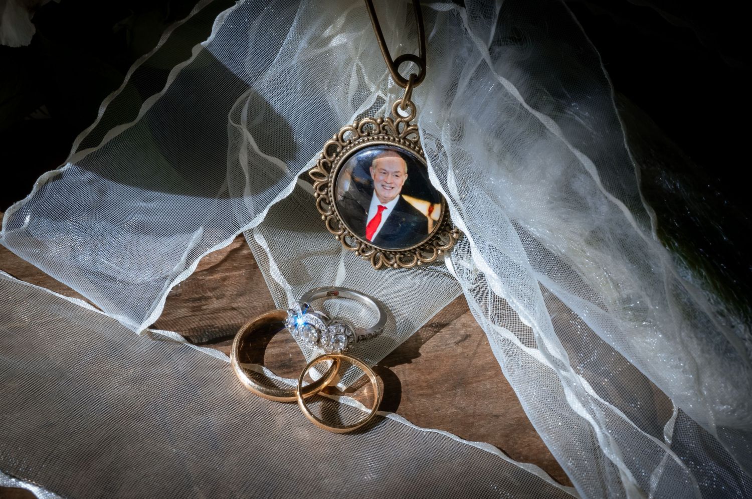 Wedding rings and a memorial photo pendant on a lace veil, honoring a loved one.