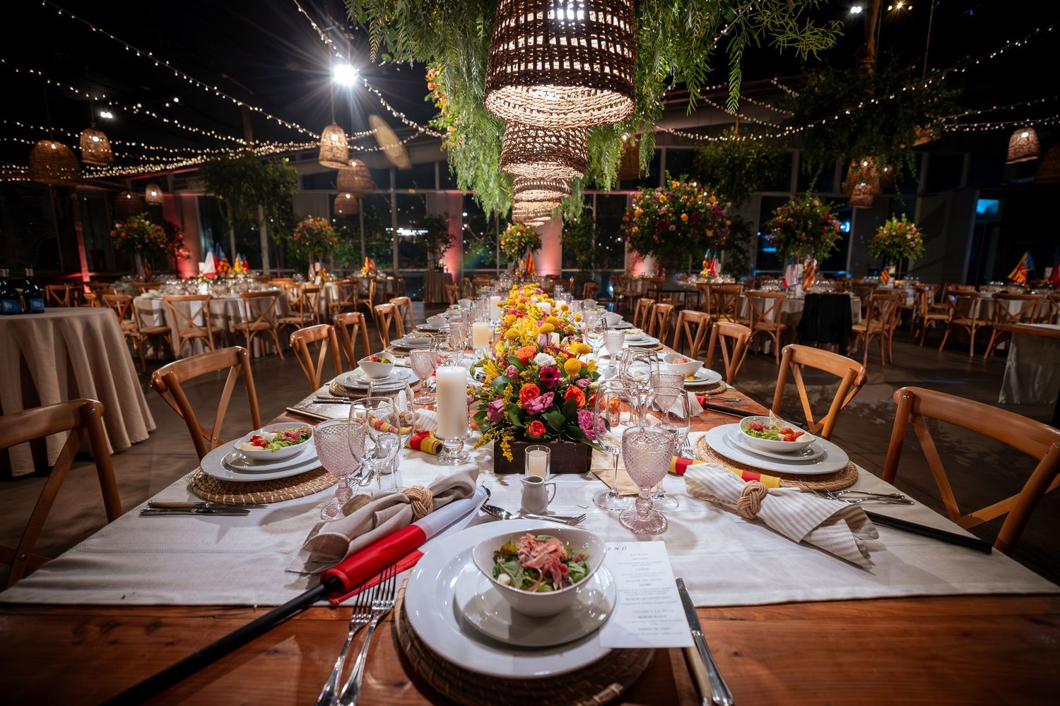 Elegantly decorated wedding reception tables with colorful floral centerpieces under warm string lights.