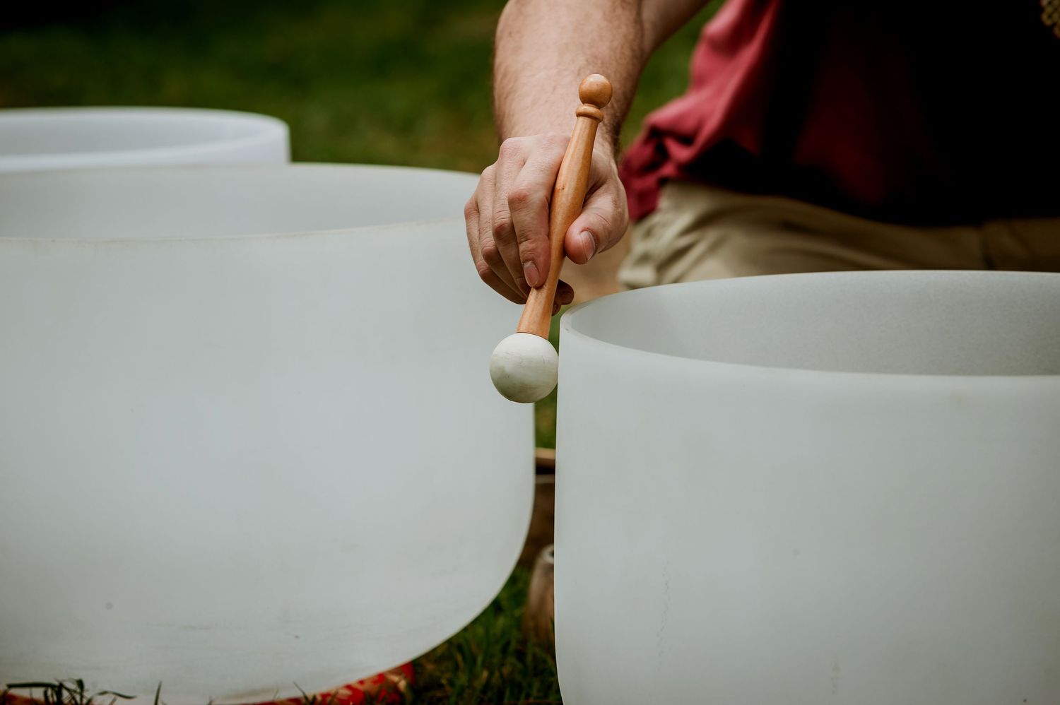 Person playing crystal singing bowls outdoors with a mallet, creating healing sound therapy music.
