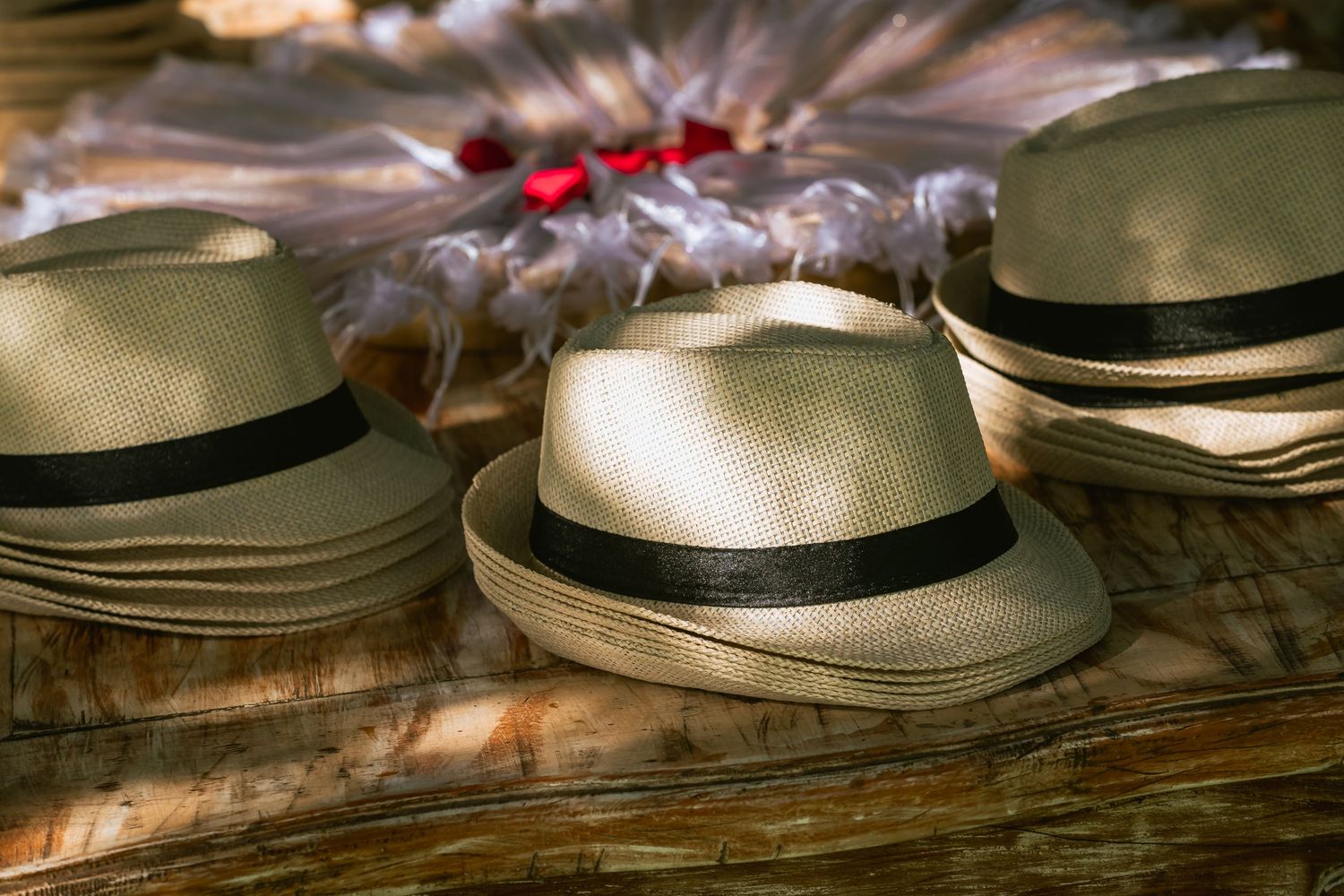 Stack of cream Panama hats with black bands displayed on wooden surface at wedding reception.
