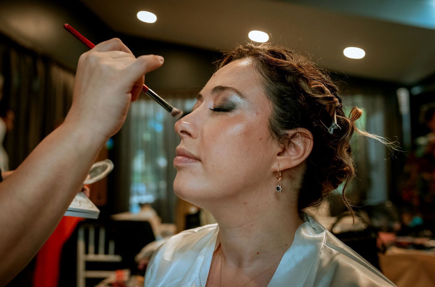 Professional makeup artist applying eyeshadow to a bride during wedding day preparation indoors.