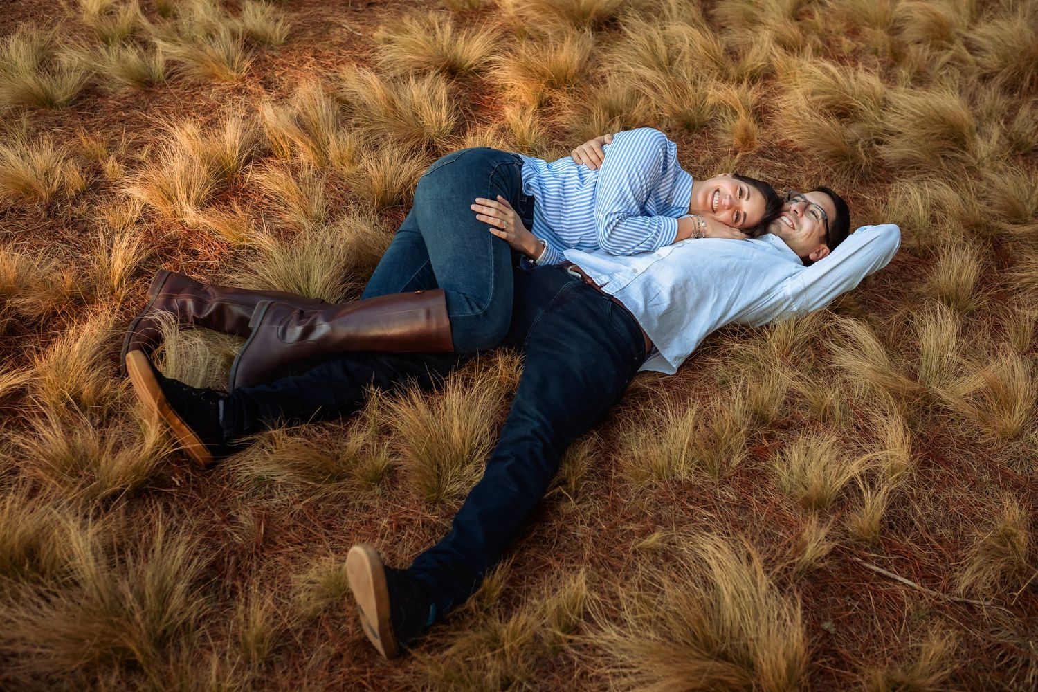 A couple lying together in a field of golden dry grass, relaxing and enjoying each others company.