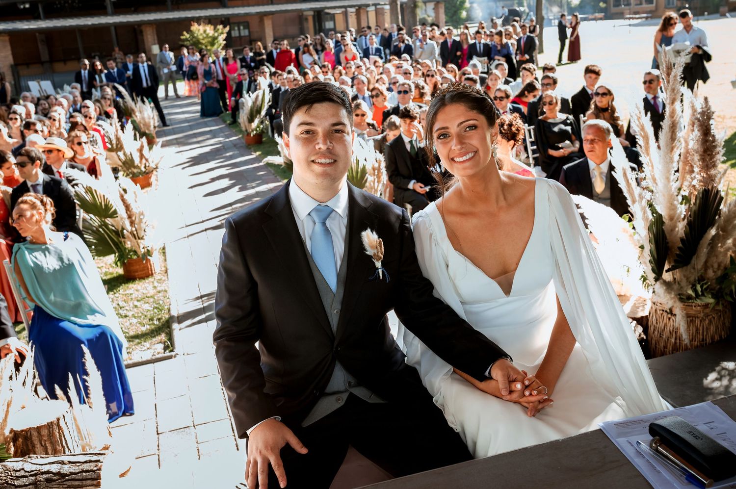 Smiling bride and groom sit together at outdoor wedding ceremony altar.