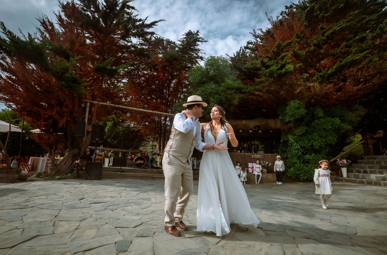 Bride and groom share a joyful dance on a stone patio surrounded by colorful autumn trees at their wedding.