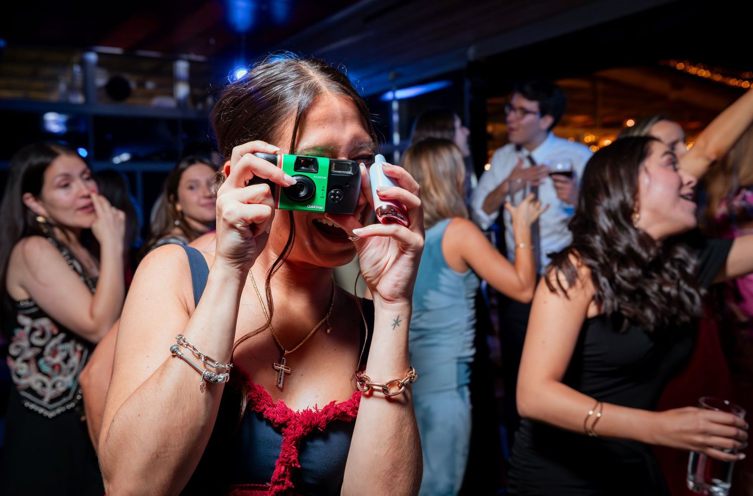 Wedding guest takes a photo with a disposable camera on the dance floor during a festive reception party.