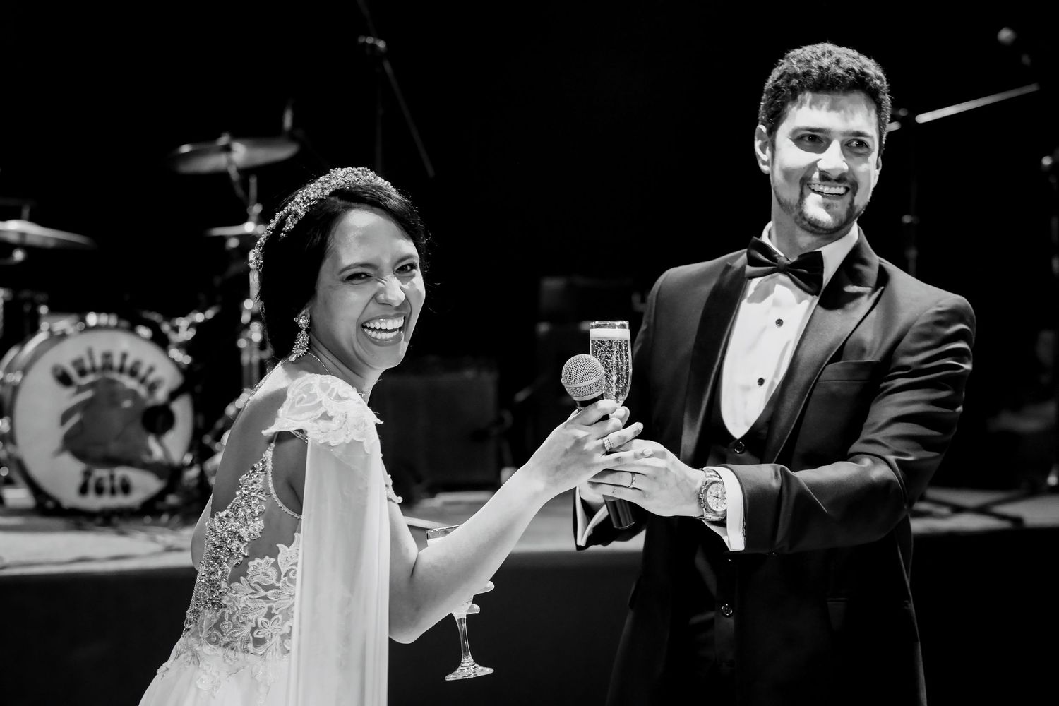 Smiling bride and groom toasting with champagne glasses at wedding reception with live band stage.