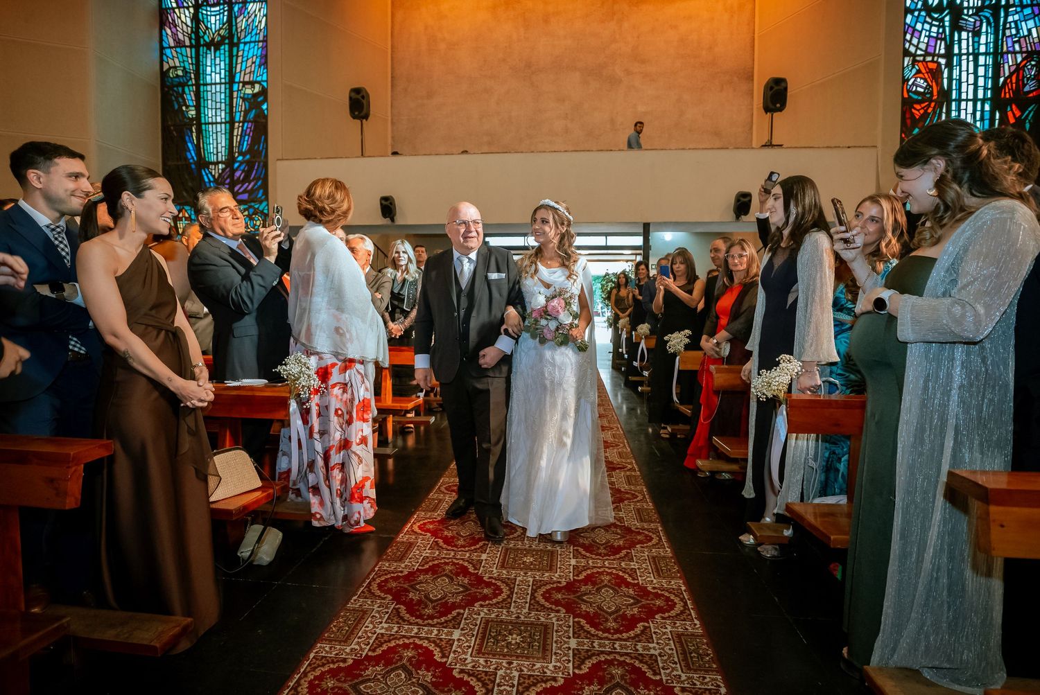 Bride walks down the church aisle with an older man as guests celebrate on both sides.