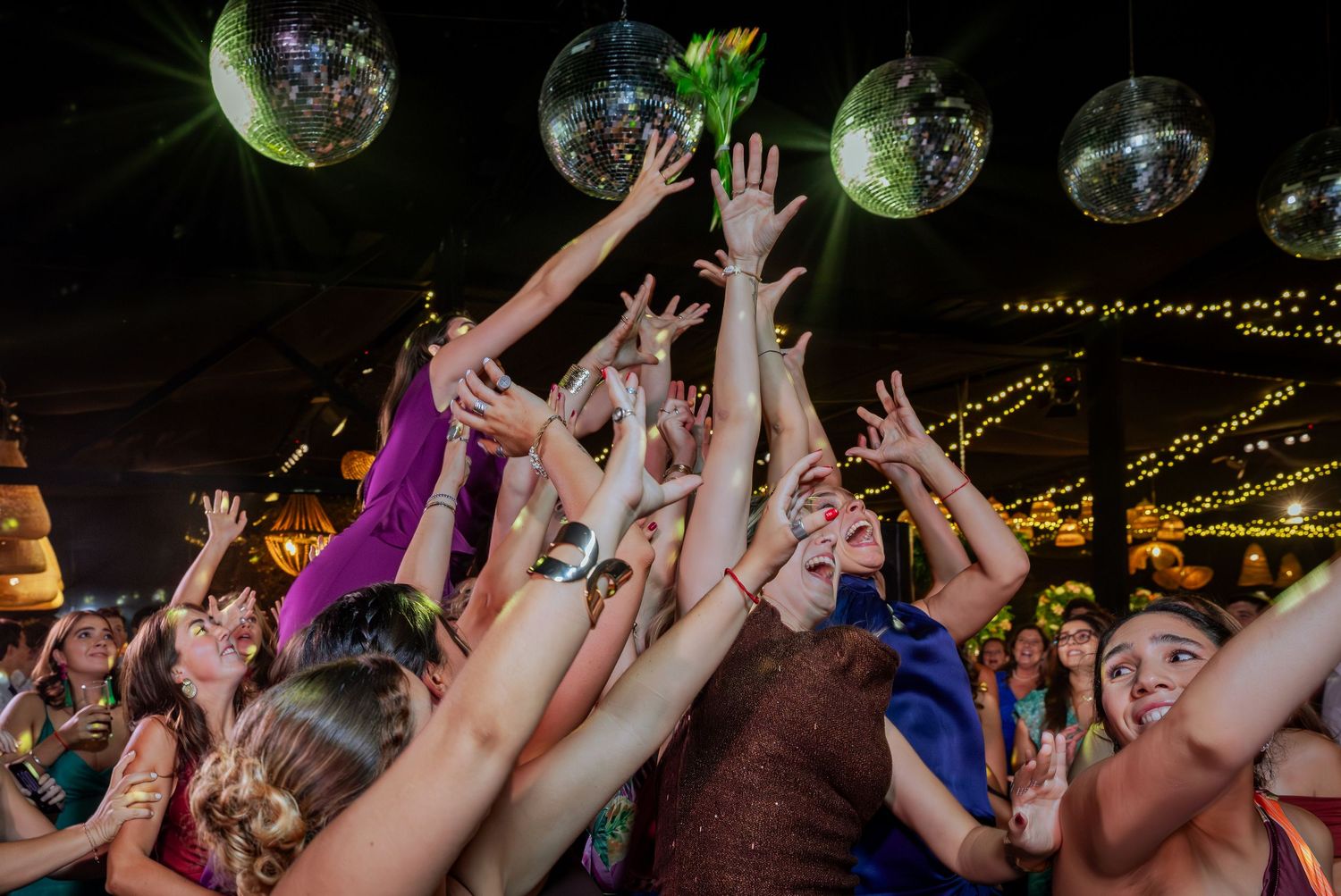 Wedding guests reach up toward disco balls on decorated dance floor at reception.