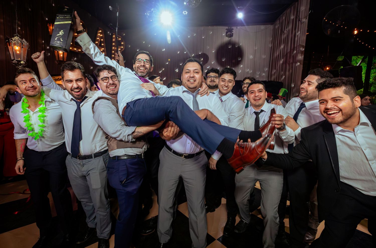 Groomsmen lift groom in air during fun wedding reception celebration with confetti.