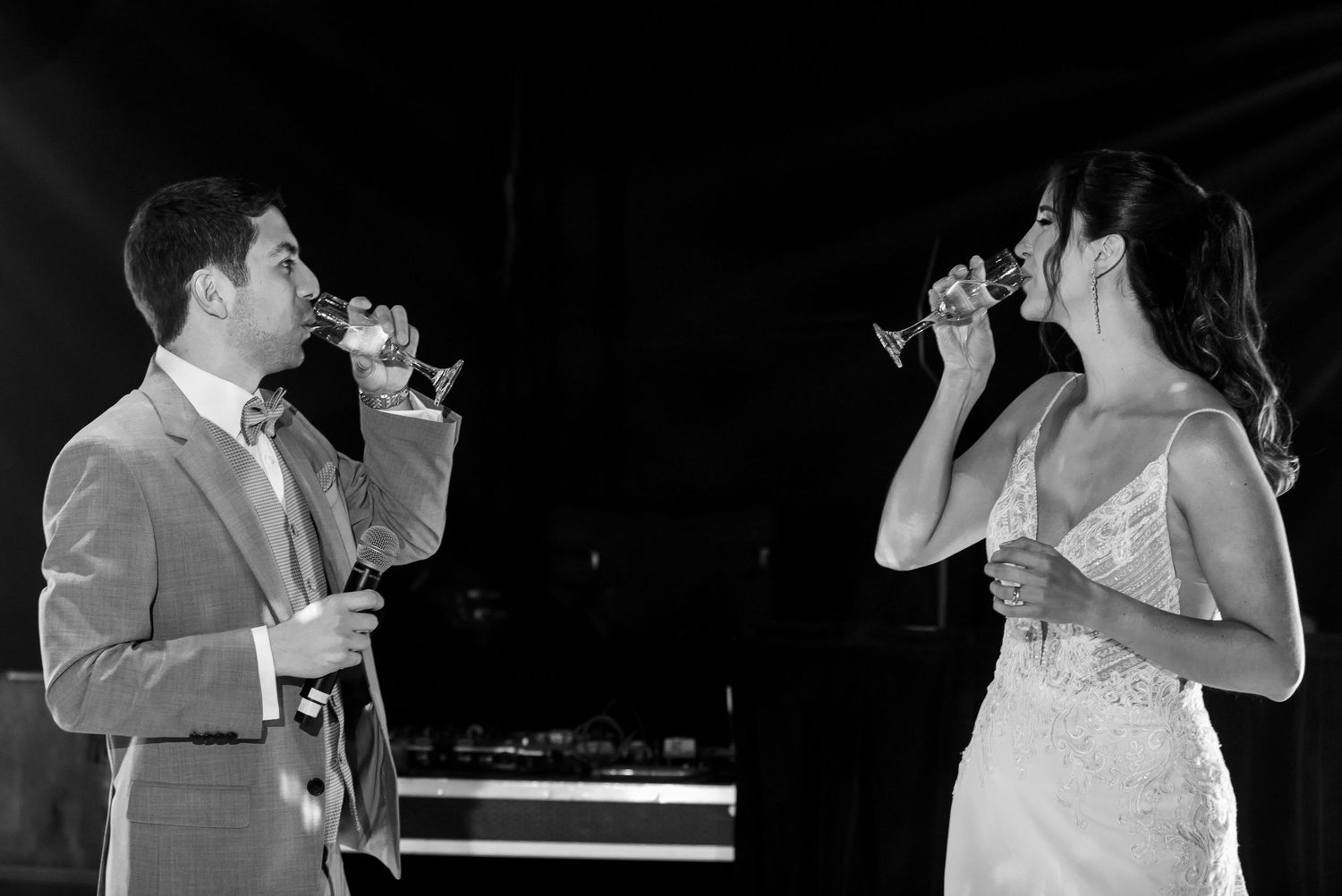 Black and white photo of bride and groom toasting with champagne glasses at their wedding reception.