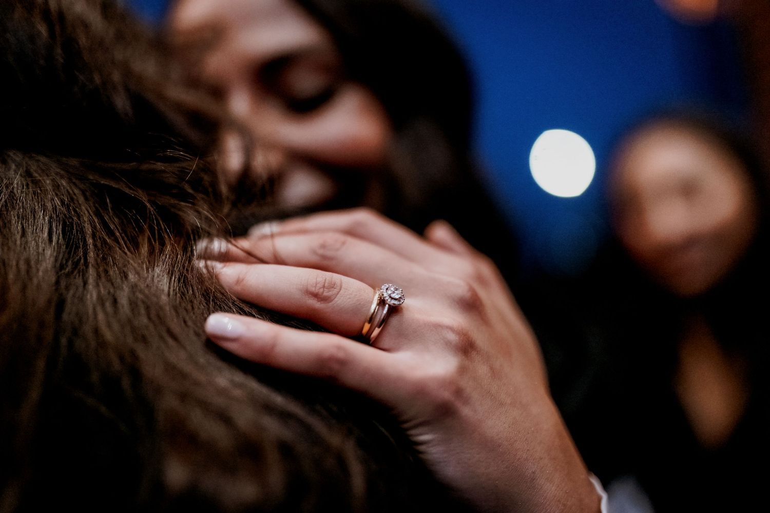 Close-up of a hand with an engagement ring resting on someone's hair during a romantic moment.