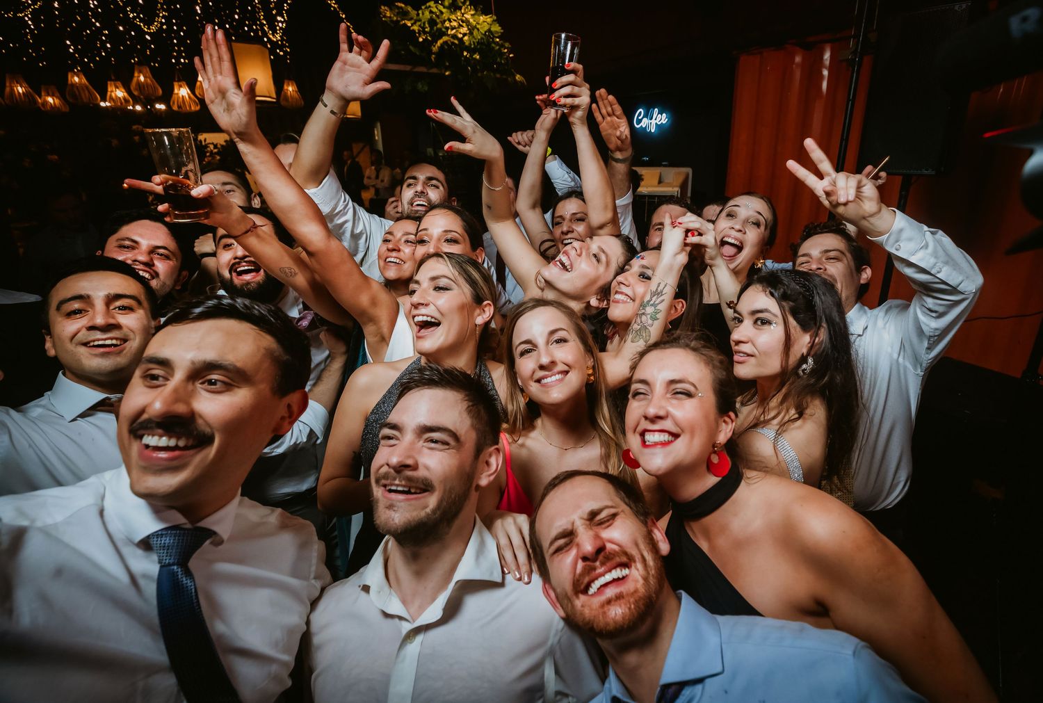 Large group of happy people taking a fun selfie at a lively wedding reception party at night.