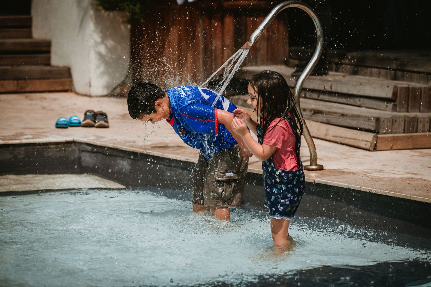 Two children playing in a shallow pool with a water fountain on a warm summer day.