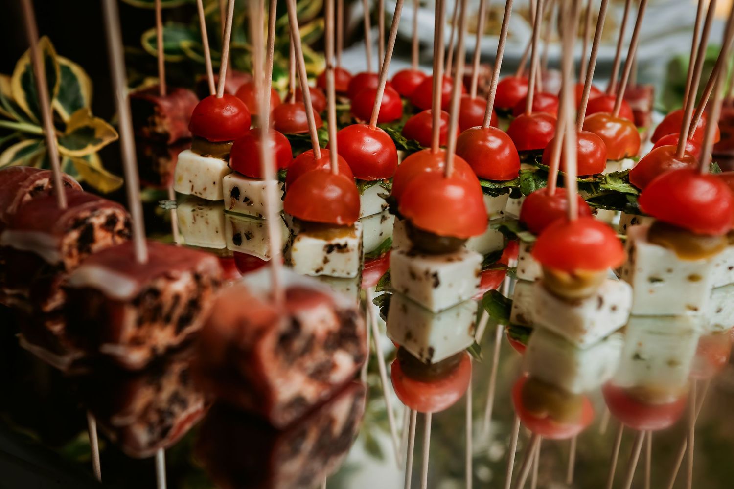 Elegant appetizer skewers with cherry tomatoes and feta cheese displayed on a catering table at an event.