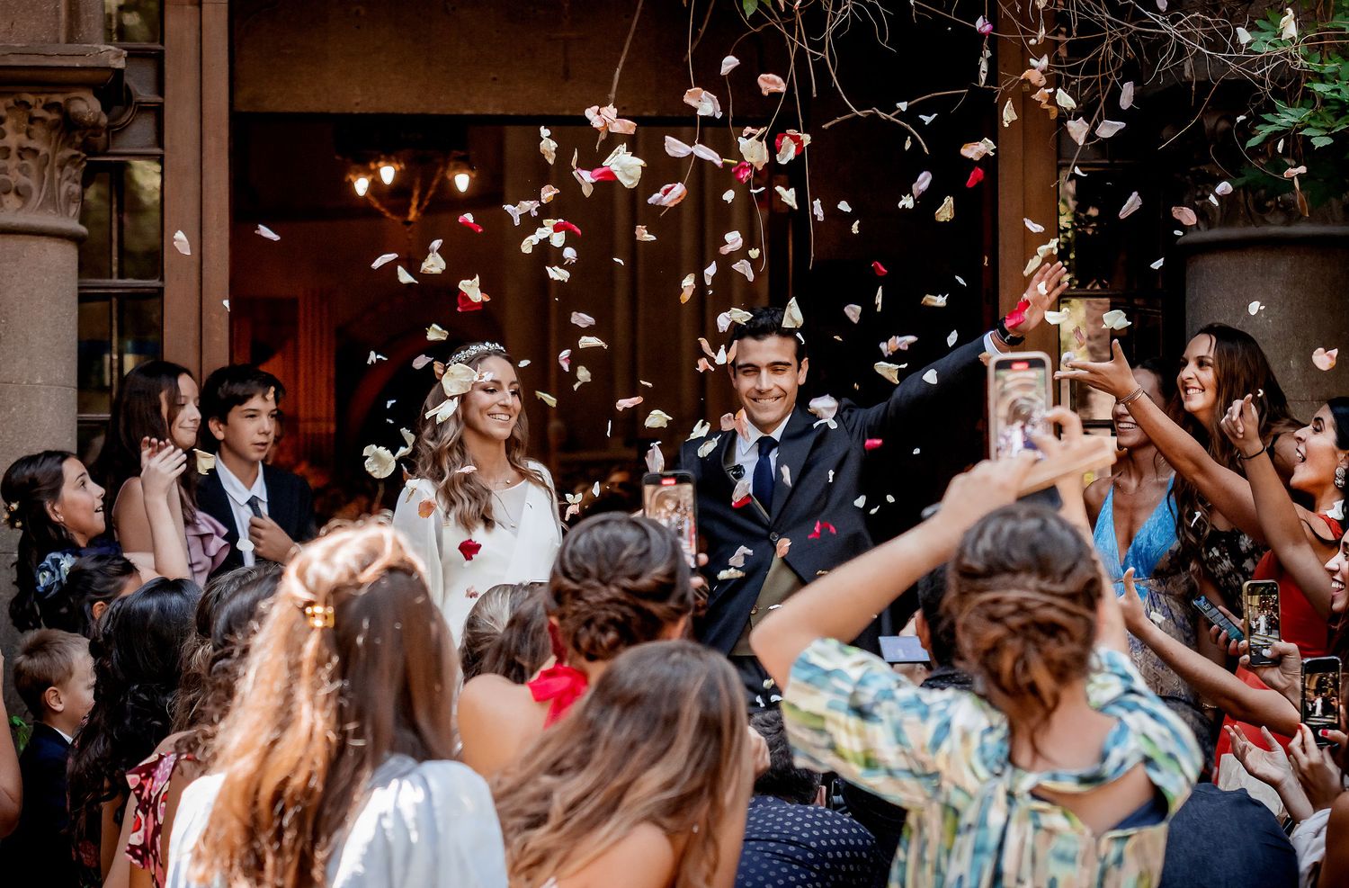 Newlyweds exit ceremony as guests toss flower petals in joyful wedding celebration.