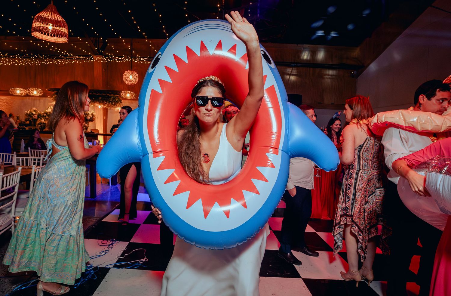 Bride dancing in inflatable shark pool float at wedding reception party.