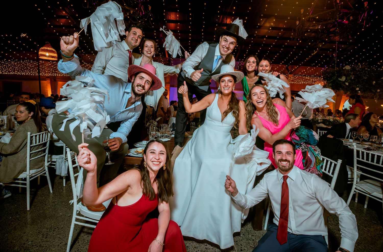 Bride lifted by celebrating wedding guests waving white napkins at lively reception.