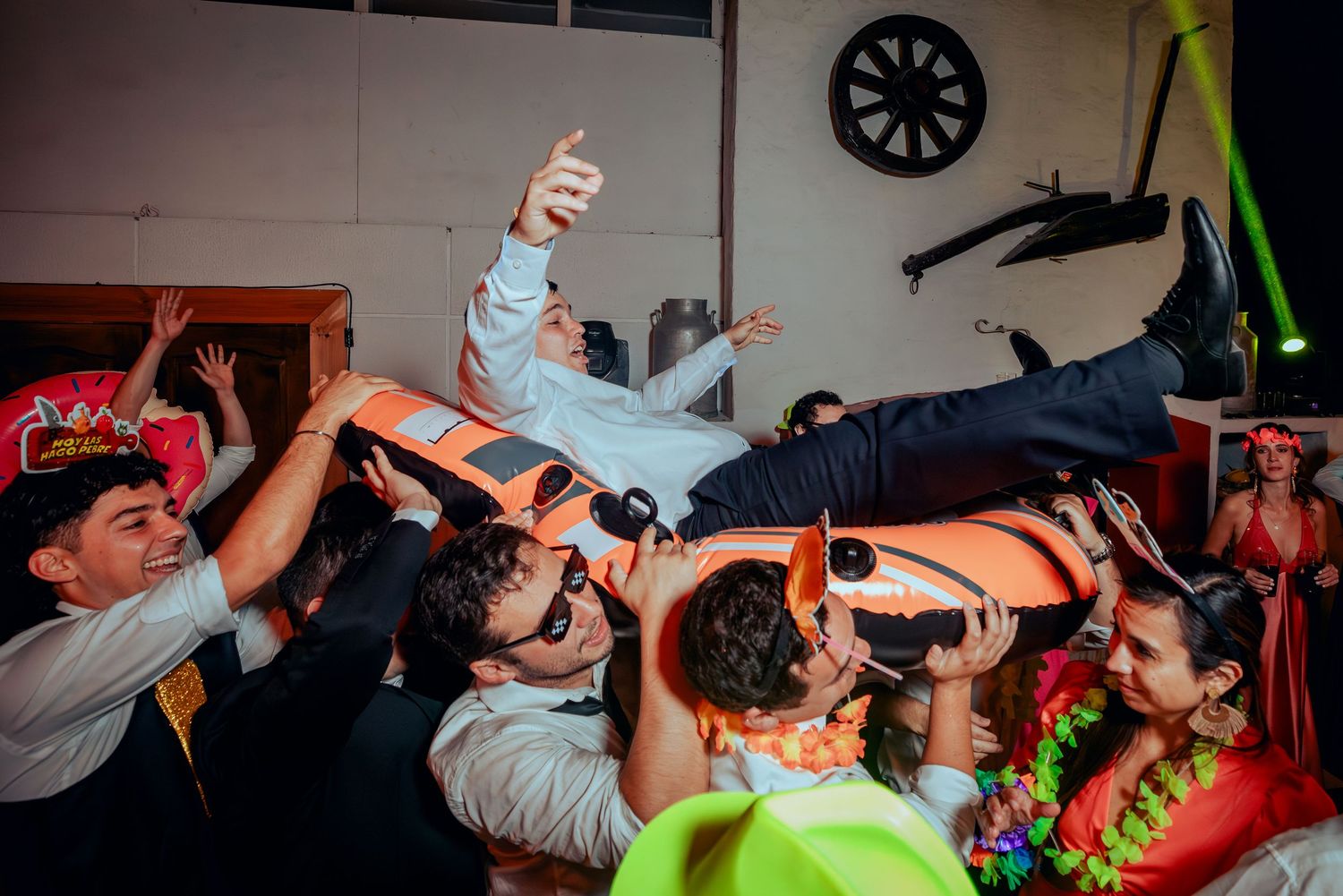 Groom being lifted by guests at energetic wedding reception celebration.
