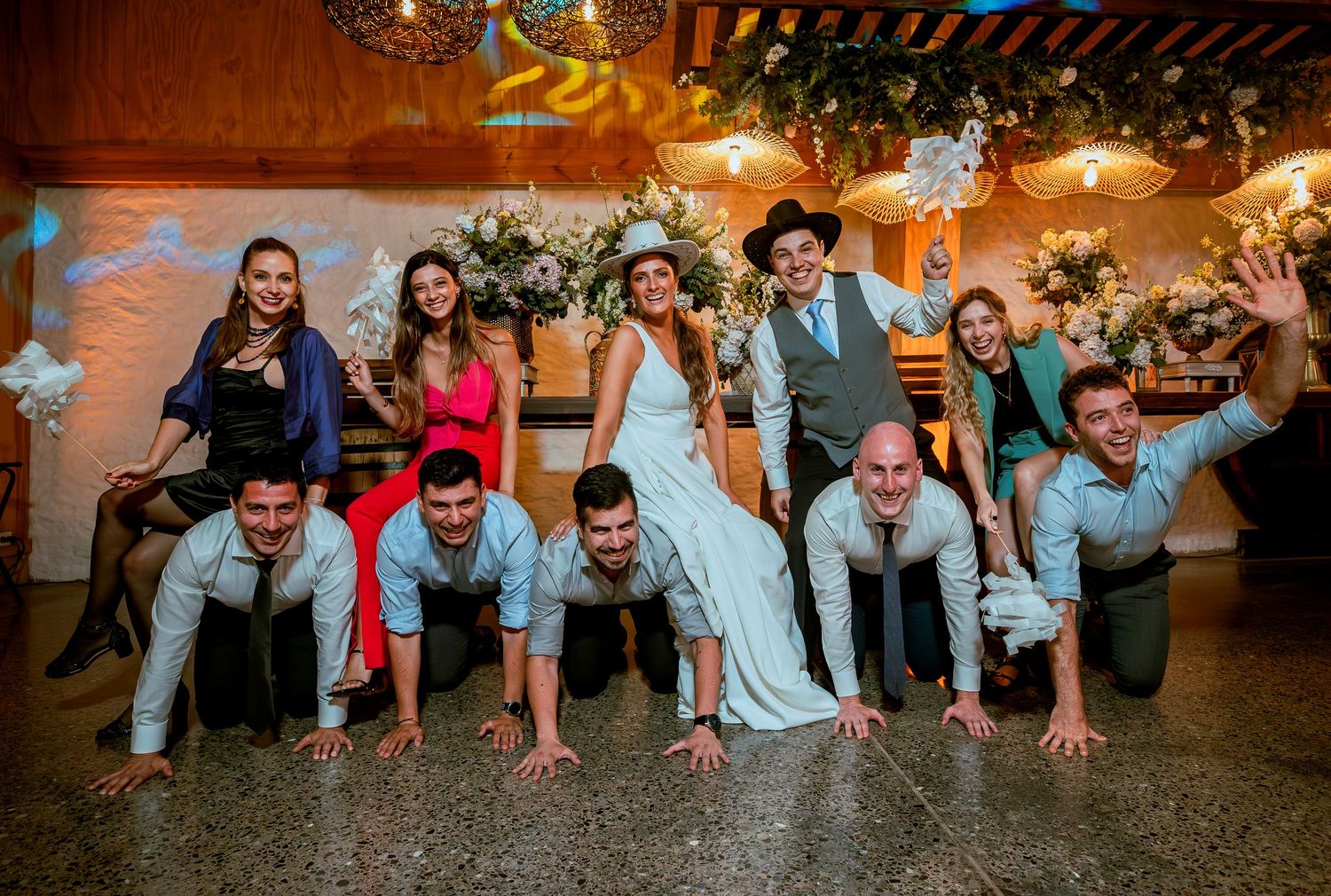 Groomsmen do push-ups while bride and groom pose with wedding party on dance floor.