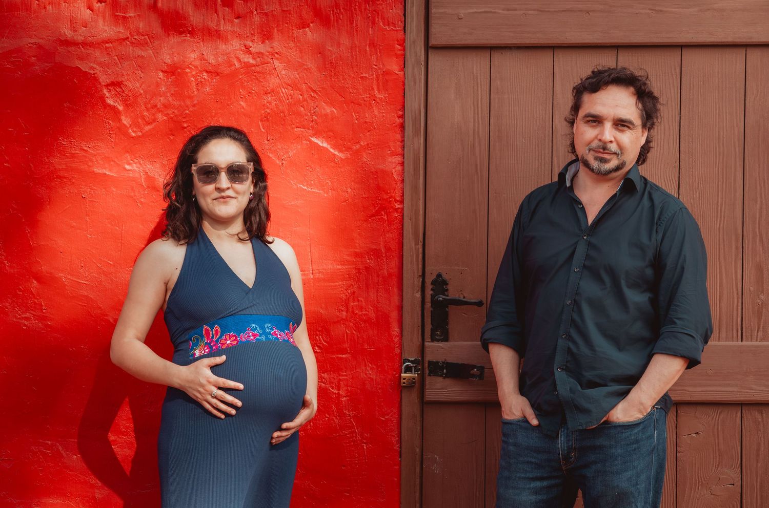 Pregnant woman and man posing separately against a bold red wall and door.