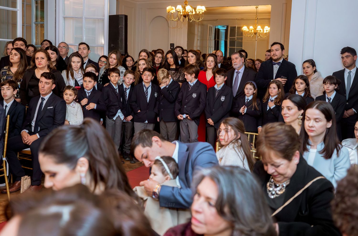 Large group of students in school uniforms and adults gathered in an elegant hall during a formal ceremony.