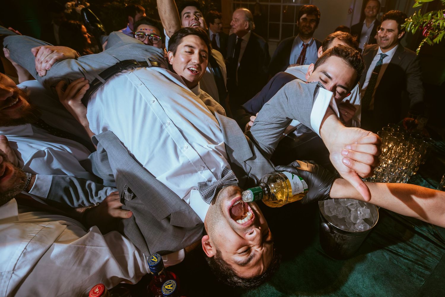 Groomsmen celebrating at a wedding reception, pouring drinks in a lively party moment.