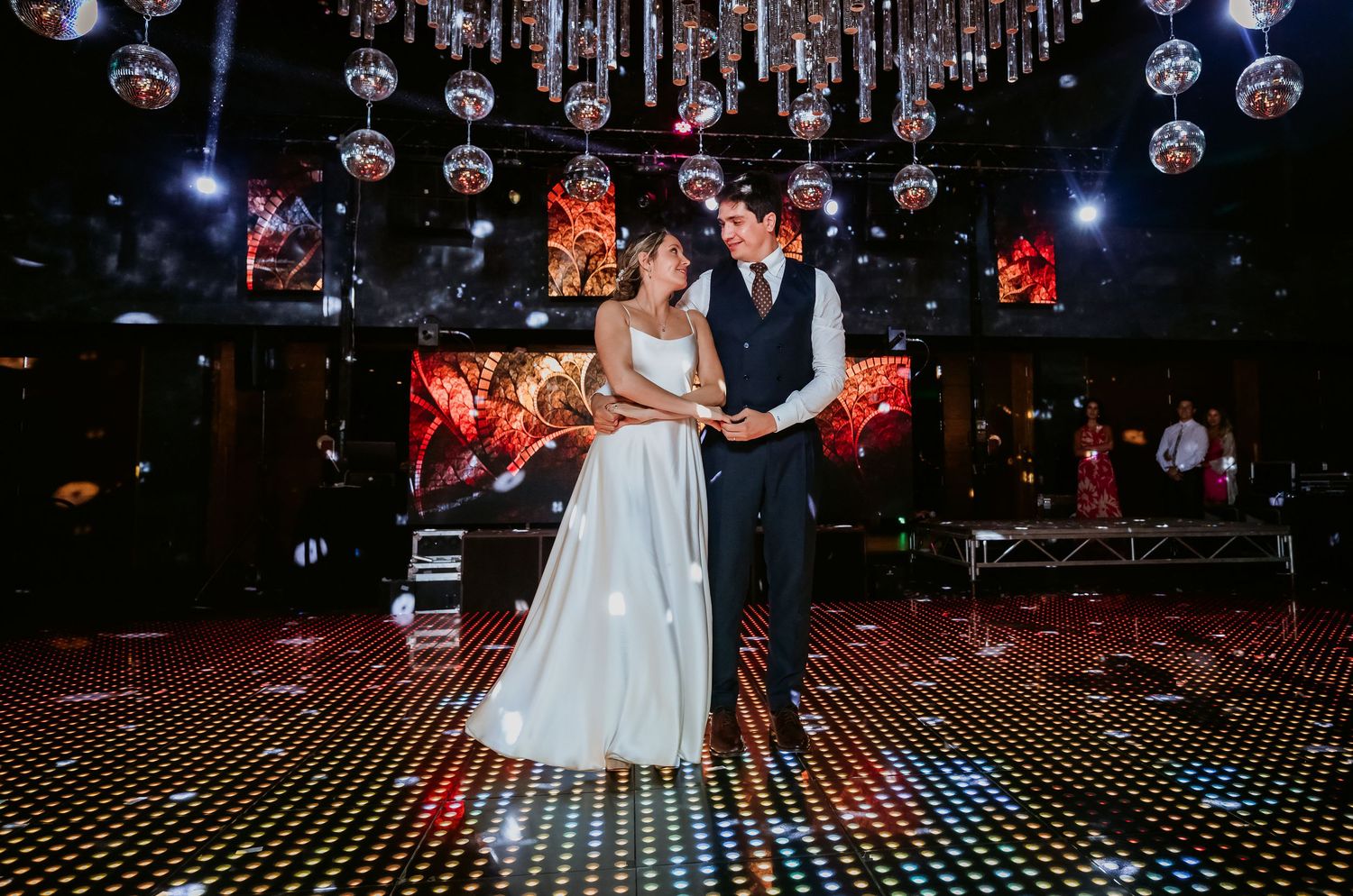 Bride and groom share intimate dance on star-lit dance floor surrounded by disco ball decorations.
