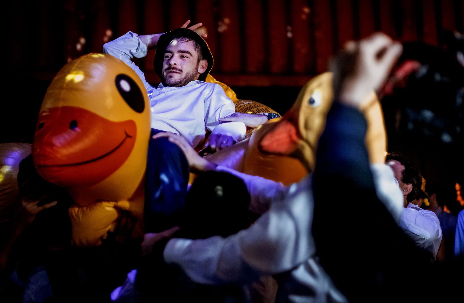 Man crowd surfing among giant inflatable rubber ducks at a lively concert event.